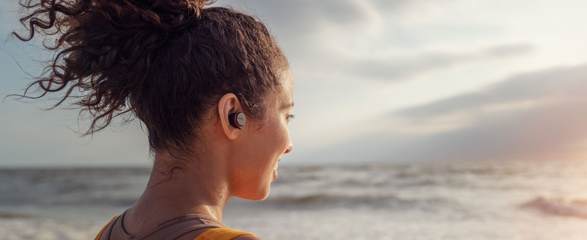 Žena koristi potpuno bežične slušalice pored mora